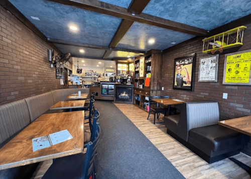 Cozy café interior with wooden tables, brick walls, and a counter displaying drinks and snacks.